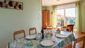 Een eetruimte met een tafel voor vier personen, stoelen, een houten kast en uitzicht op de omgeving via een schuifdeur.