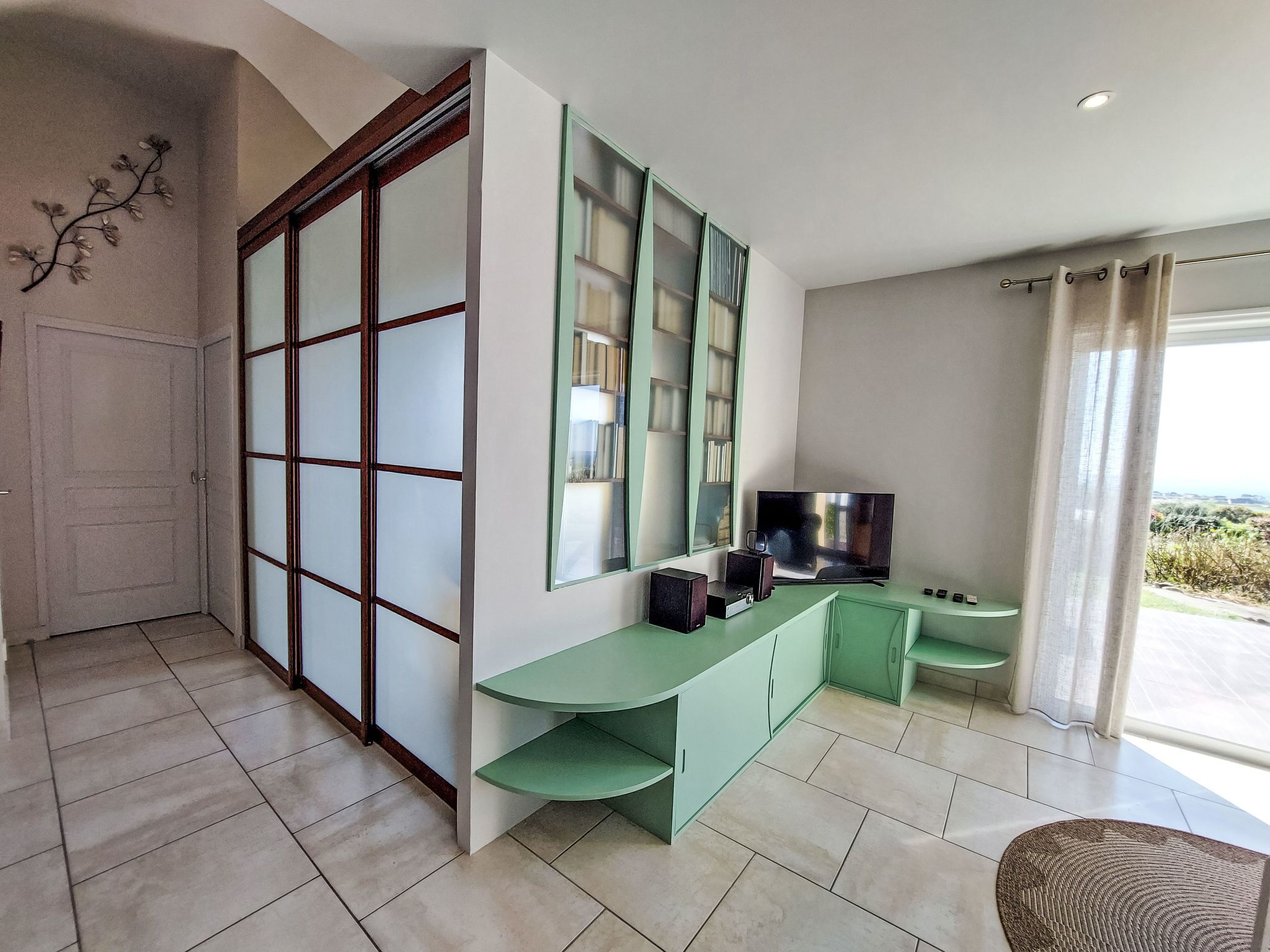 Un salon moderne doté d’une porte-fenêtre coulissante, d’un grand téléviseur à écran plat et d’une console verte.