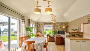 A modern kitchen with a dining area, large windows, and a stone wall. - Vacation home Orphée by Interhome (Telgruc sur Mer)