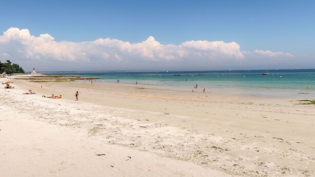 Une plage avec un phare, un ciel dégagé et une mer calme.