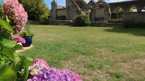 Une structure historique en pierre, dotée d’arches et de vestiges, entourée d’une pelouse bien entretenue et de plantes en fleurs.