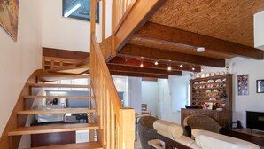 Eine Holztreppe führt zu einem Wohnbereich mit einer Couch und einem Esstisch.