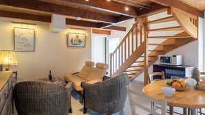 Ein gemütliches Wohnzimmer mit einer Holztreppe, Korbsesseln, einem Esstisch mit Obst und Kunstwerken an den Wänden.