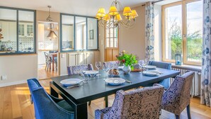 A dining area with a large table set for six, surrounded by patterned chairs. A chandelier hangs above, and a vase with flowers is on the table. - Balade Océane by Interhome (Tregunc)