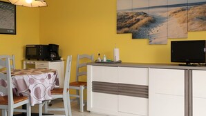 Una habitació amb parets grogues, zona de menjador, taulell de cuina i televisió.