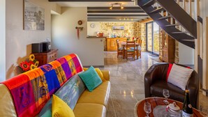 A cozy living room with a sofa, a dining area with a table and chairs, a kitchen with a stone wall, and a staircase.