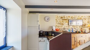 A kitchen with white cabinets, a stone wall, a clock, and a coffee maker.