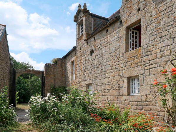 A stone building with multiple windows and a garden with various plants and flowers.