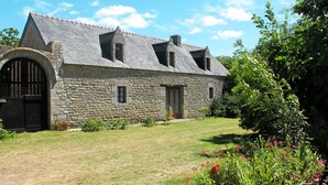A stone building with a sloped roof, a large arched entrance, and a small garden with flowers.