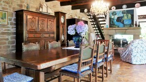 A rustic dining area with a wooden table and chairs, a large wooden cabinet, and a painting above the fireplace.