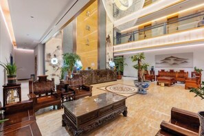 A spacious lobby with a high ceiling, a reception desk, seating area, and decorative plants. - Shengtong Hotel (Lijiang)