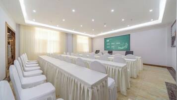 Un salón de conferencias con una larga mesa, sillas, una pantalla de proyector y una pizarra.