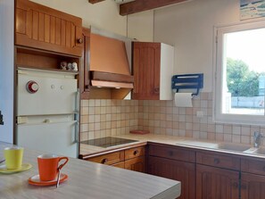 Une cuisine avec des meubles en bois, un réfrigérateur blanc, une cuisinière et une fenêtre donnant sur un paysage verdoyant.