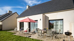 A modern house with a deck, outdoor furniture, and a barbecue grill.