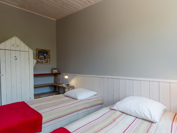 Une chambre avec deux lits, une armoire en bois, une petite table et une étagère fixée au mur.
