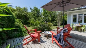 Eine Holzterrasse mit roten Adirondack-Stühlen, einem Tisch mit Stühlen und einem großen Sonnenschirm.