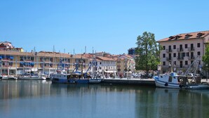 A marina with boats docked, buildings with balconies, and a clear blue sky. - Belvedere Pineta Camping Village by Interhome (Grado)