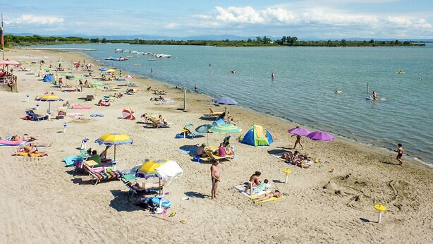A beach with numerous umbrellas and sun loungers, a sandy shore, and calm water. - Belvedere Pineta Camping Village by Interhome (Grado)