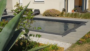 Ein Pool mit Liegestühlen, umgeben von Pflanzen und einem Gebäude mit Fenstern.