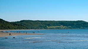 Ein Strand mit Menschen, ein bewaldeter Hügel und ein klarer Himmel.