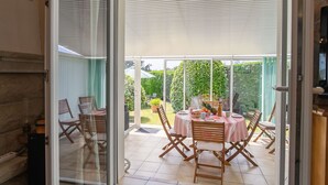 A patio area with a table set for dining, surrounded by wooden chairs, and a view of a garden. - Gueradur by Interhome (Pleumeur Bodou)