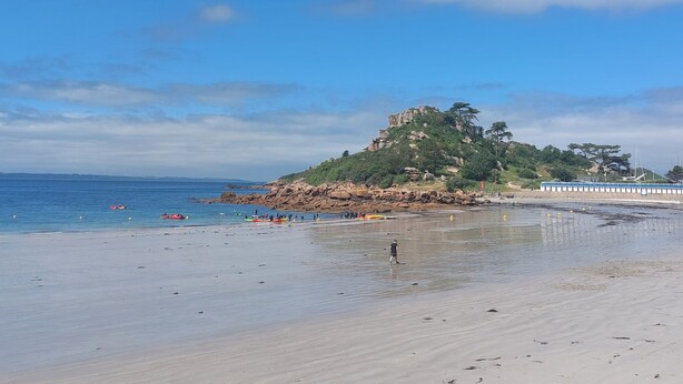 Una playa con un promontorio rocoso, mar tranquilo y cielo despejado.