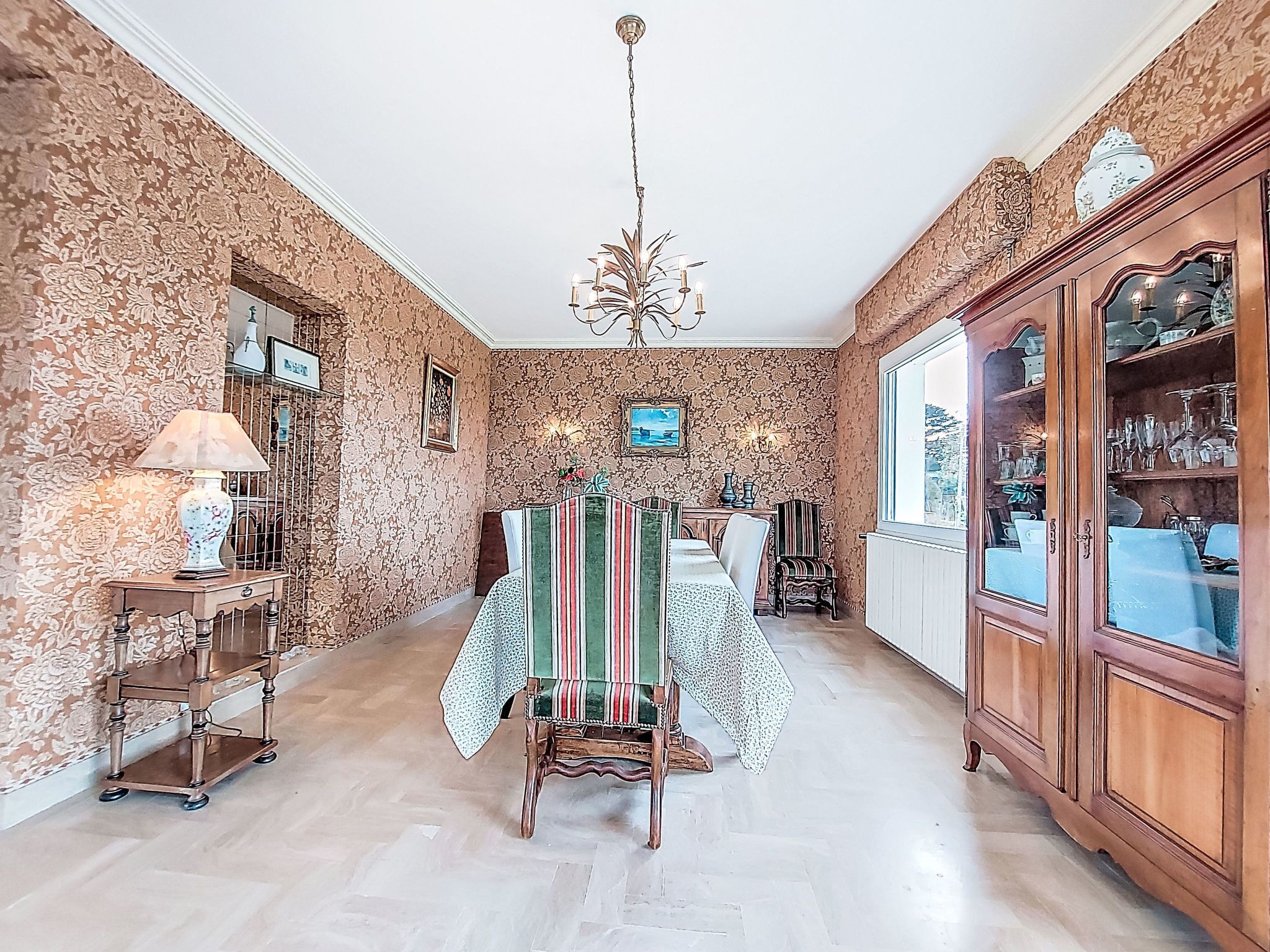 A dining area with a table set for four, a chandelier, and a cabinet with glassware.