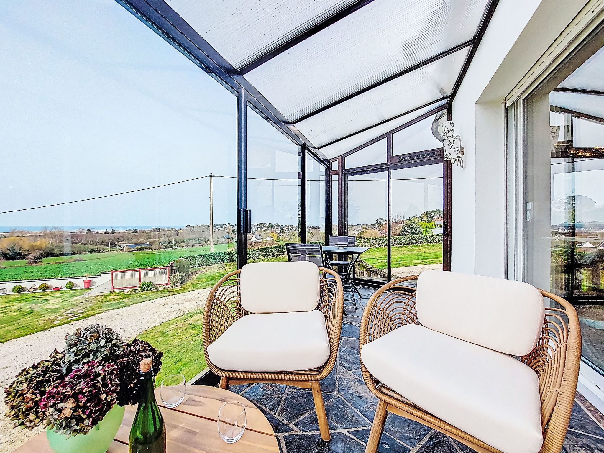 A conservatory with wicker chairs and a table, overlooking a green landscape.