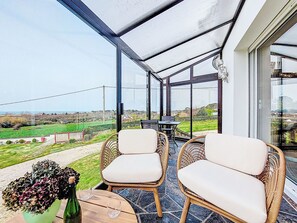 Un invernadero con sillas de mimbre y una mesa, con vistas a un paisaje verde.