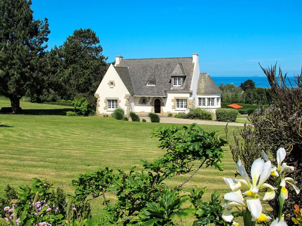 A large house with a well-maintained lawn and garden, a clear view of the sea, and a prominent tree in the foreground. - La Rotonde by Interhome (Penvénan)