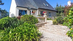 A stone house with a steep roof, a front porch with a railing, and a staircase leading to the entrance. - Les Courlis by Interhome (Trévou-Tréguignec)