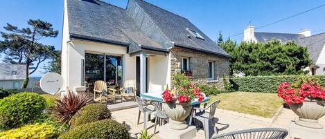 A house with a stone exterior, a large patio with outdoor furniture, and a garden with various plants and flowers.