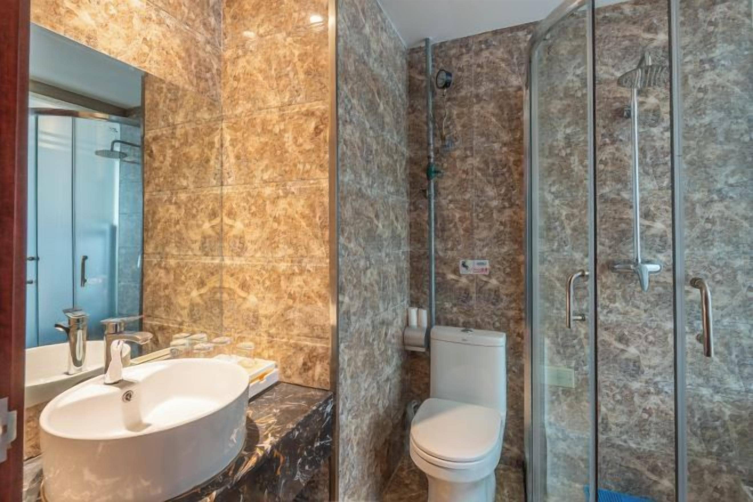Un baño con lavamanos de mármol, inodoro y cabina de ducha con paredes de vidrio.