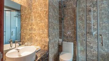 Un baño con lavamanos de mármol, inodoro y cabina de ducha con paredes de vidrio.