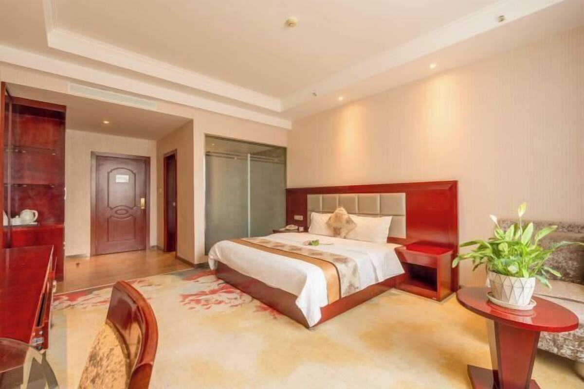 Een hotelkamer met een bed, nachtkastje, stoel en een tafeltje met een plant.