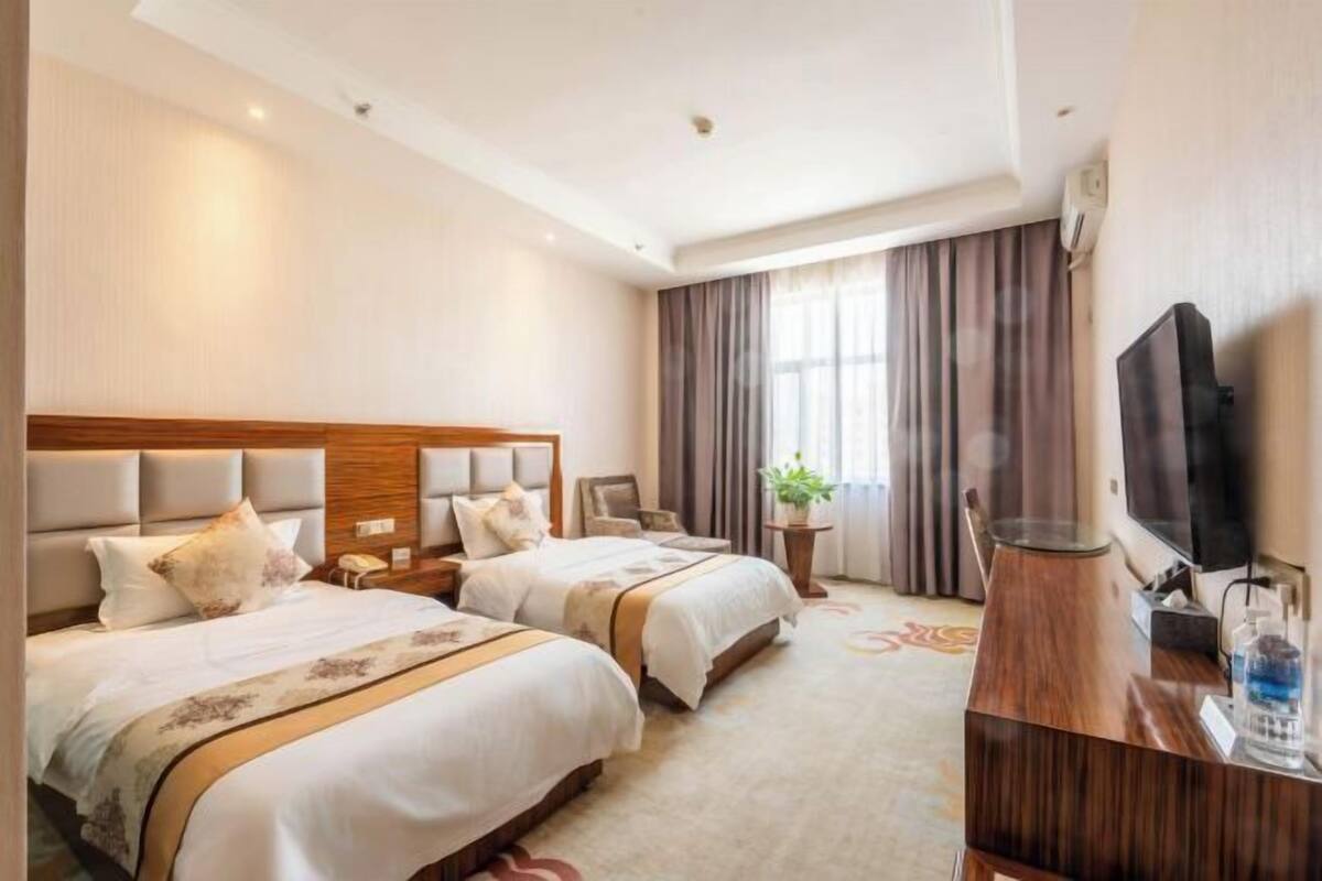 Een hotelkamer met twee bedden, een televisie, een bureau en een raam met gordijnen.