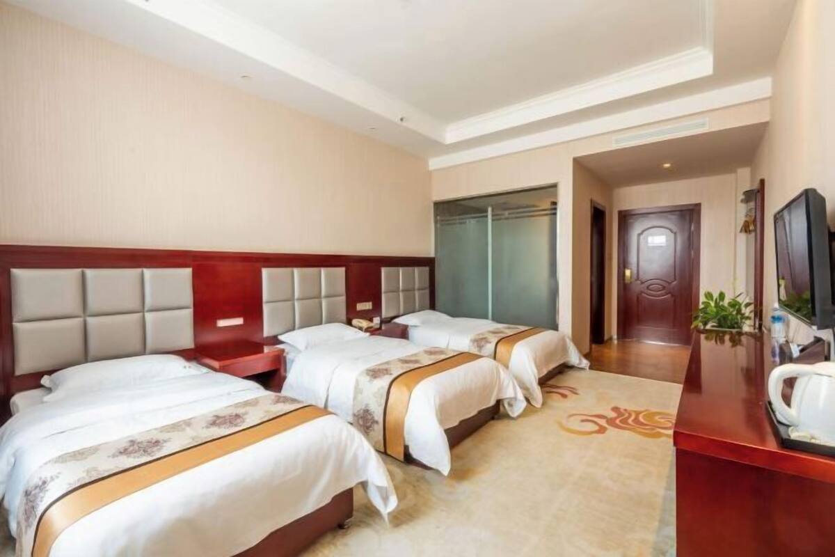 Een hotelkamer met twee bedden, een houten hoofdbord, een bureau met een televisie en een deur naar een andere kamer.