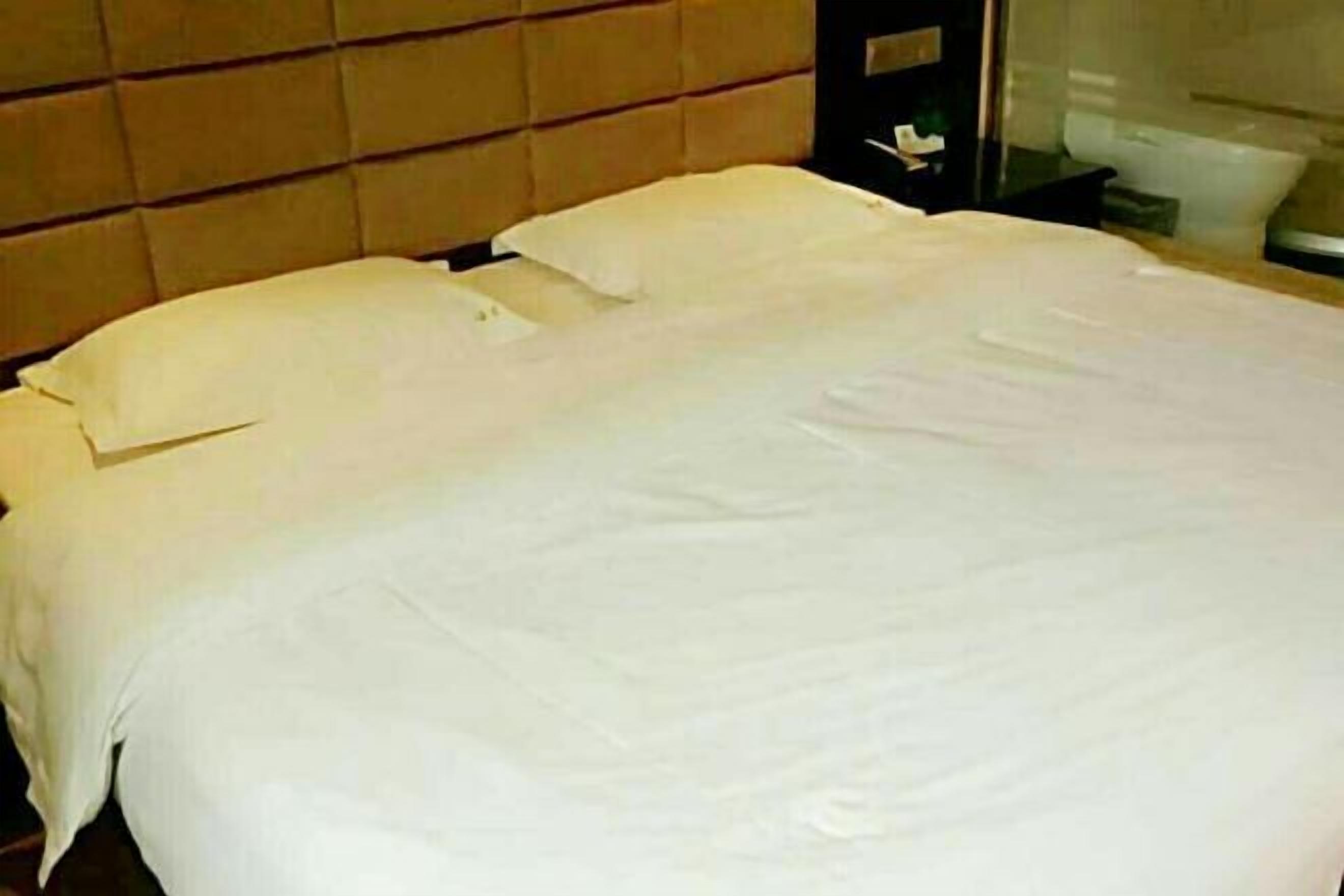 A neatly made bed with white linens, a headboard, and a bedside table with a lamp.