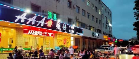 Un restaurante con terraza, alfombra roja y un edificio de varios pisos y ventanas.
