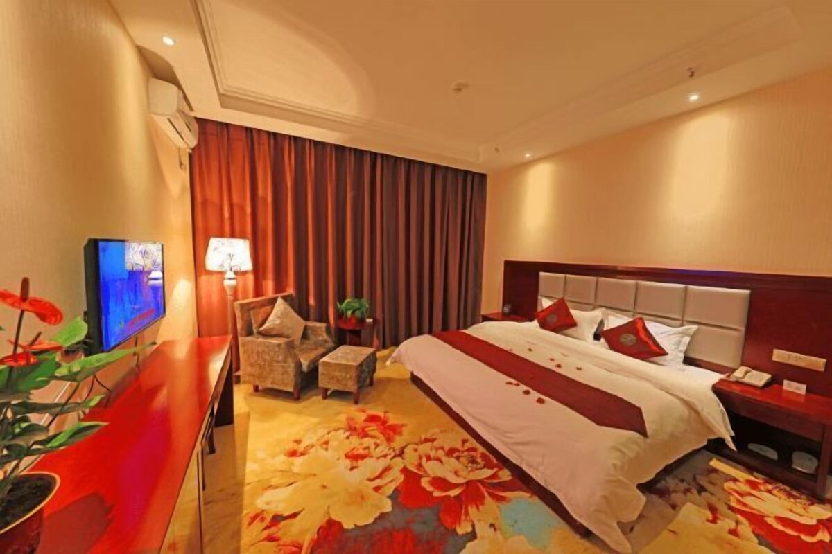 A hotel room with a large bed, a flat-screen TV, a desk with a chair, and a floral carpet.