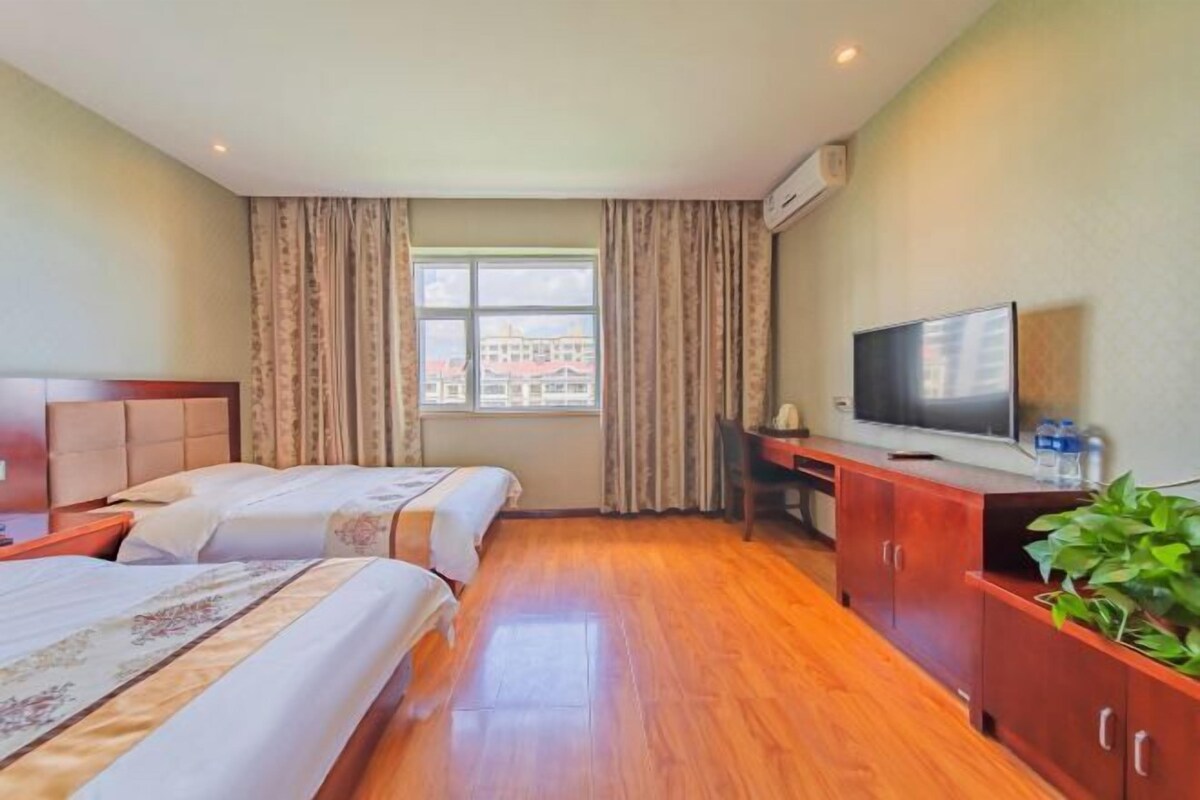 A hotel room with two beds, a TV, a desk, and a window with curtains.