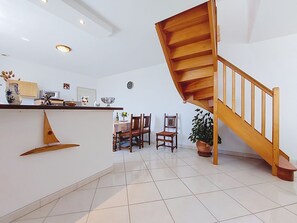 Une cuisine moderne avec un escalier en bois, un coin repas avec des chaises et une table, et une plante en pot.