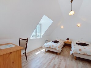 Une chambre avec deux lits, un bureau, une chaise, une fenêtre et un plafond en pente.