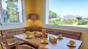A wooden dining table with yellow cups and a loaf of bread, set in a corner with a view of greenery and buildings. - de la Plage by Interhome (Pleubian)