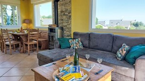 A cozy living room with a grey sofa, wooden dining table, and a stone fireplace. - de la Plage by Interhome (Pleubian)