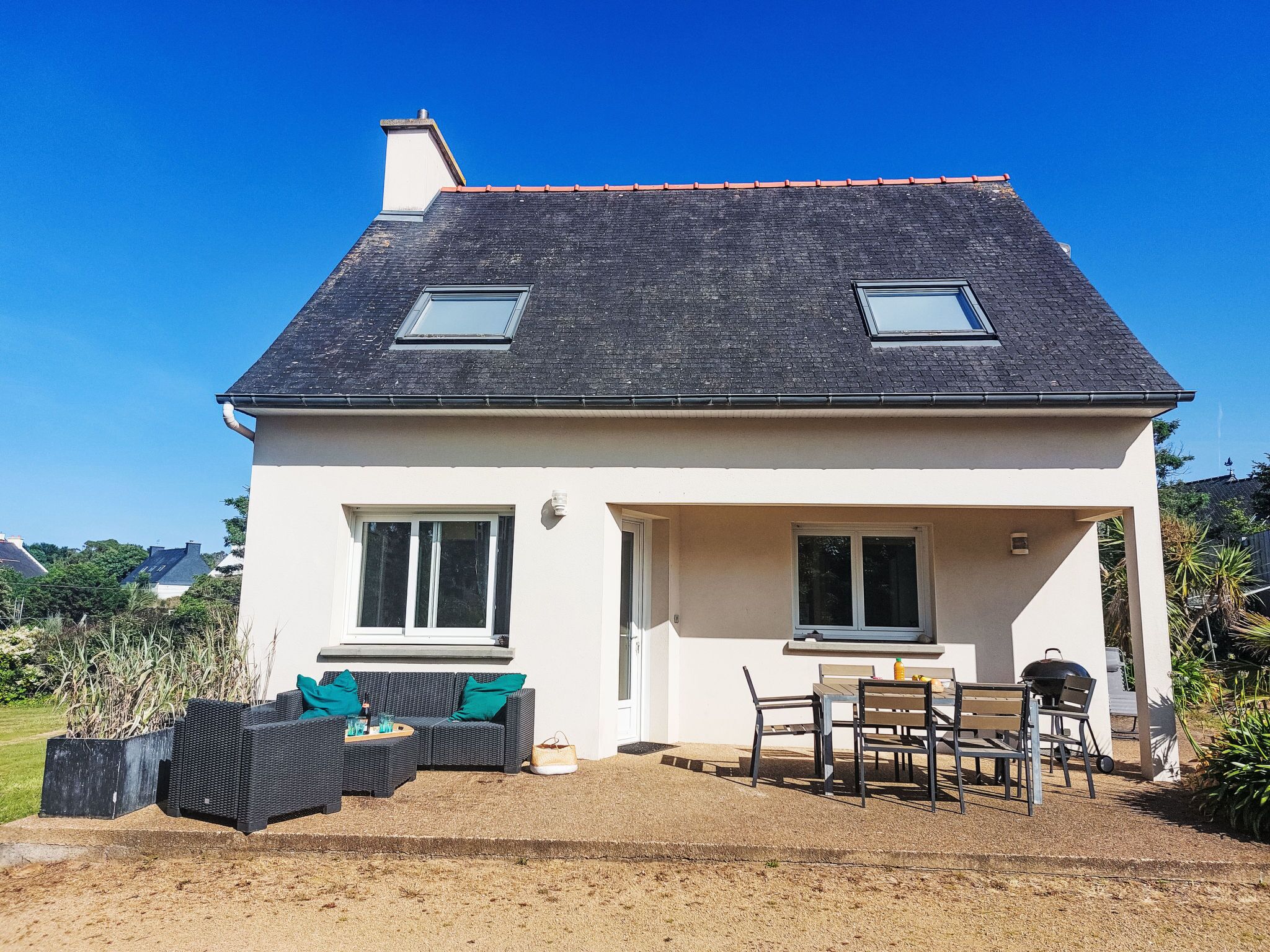 Een tweelaags huis met een schuin dak, twee dakramen, een terras met tuinmeubilair en een barbecue.