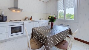 Une cuisine de taille réduite, avec des meubles blancs, une cuisinière à gaz et une fenêtre agrémentée de rideaux à motifs.