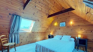Une chambre confortable avec un plafond en bois, un lit avec une literie blanche, une chaise et des lampes de chevet.