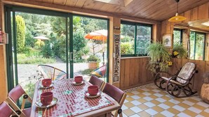 A wooden interior with a checkered floor, a table with red cups, and a view of a garden through large windows.