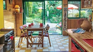 A kitchen with a tiled floor, wooden cabinets, a dining table with chairs, and a view of a garden through a glass door.